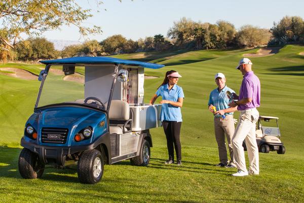 Auf einem Golfplatz steht ein Mini Food Truck. Vor dem Fahrzeug stehen mehrere Personen, die Getränke und Snacks kaufen möchten.